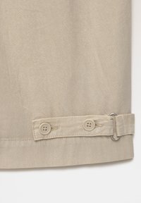 Tissu beige avec un motif à chevrons subtil, doté de deux boutons et d'un détail de boucle à l'ourlet pour un ajustement flexible.