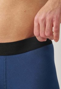 Collants bleu marine avec une texture douce, dotés d'une ceinture élastique noire. Le vêtement est ajusté et présente un détail de couture lisse.