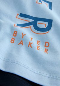 Helehall sinine T-särk oranži ja sinise graafikaga. Tekstil "BYTED BAKER" ning stiliseeritud logo. Sile tekstuur, istuv lõige.