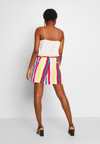 Jupe courte rayée avec des couleurs vives de rose, jaune, bleu et rouge ; tissu doux avec une coupe décontractée et des poches, portée avec un haut beige.