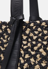 Sac à main tissé comprenant des matériaux noirs et marron clair, des lanières en cuir et une surface texturée. Remarquable pour son design tressé et ses couleurs contrastantes.