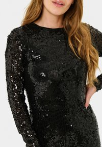 Rochie neagră din paiete cu mâneci lungi, având o suprafață texturată și o gât cu decolteu rotund, care oferă un aspect strălucitor.