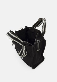 Borsa a spalla nera in canvas con chiusura a zip, dotata di manici intrecciati a righe bianche e nere e un accento in pelle liscia. Tasche interne visibili.