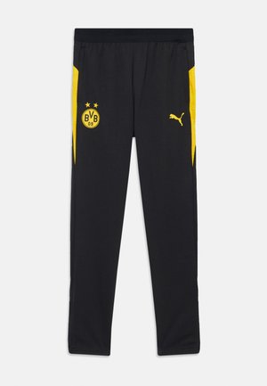 Svarte treningsbukser med gule detaljer, med en logo foran og side-striper. Laget av et lett og pustende stoff.