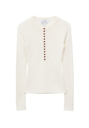 Ivory long-sleeve knit top featuring a round neckline, a button front with dark brown buttons, and side panels for a fitted silhouette.