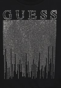 Maglietta nera con la scritta "GUESS" in grandi strass, con un design a cascata di strass più piccoli che crea un effetto luccicante.