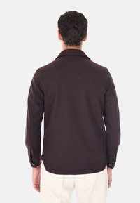 Giacca marrone con una texture morbida, maniche lunghe e colletto. Presenta polsini con bottone e una leggera fessura laterale all'orlo.