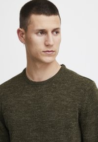 Dunkelgrüner Strickpullover mit Rundhalsausschnitt, aus strukturiertem Material; zeichnet sich durch eine figurbetonte Passform und dezente Nähte aus.