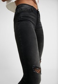 Svarta denimjeans med slim fit, slitna hål vid knäna och en slät textur med minimal detaljer och sömmar.