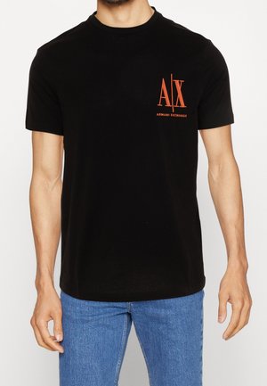 Black cotton t-shirt featuring short sleeves, rounded neck, and an orange logo on the left chest. Pair of blue jeans completes the look.
