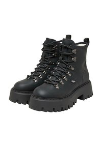 Bottines noires à lacets avec une semelle en caoutchouc épaisse, dotées d'œillets et de crochets en métal, d'une texture en cuir lisse et d'une languette à l'arrière.