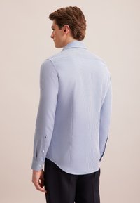Camicia a maniche lunghe a scacchi blu chiaro realizzata in tessuto intrecciato. Presenta un colletto classico e dettagli con bottoni sui polsini. Orlo curvo.