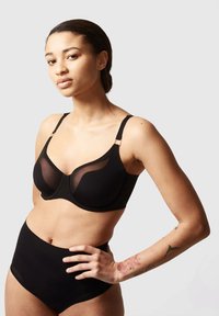 Black bra with sheer paneling and adjustable straps, featuring curved seams and a smooth finish. High-waisted black briefs shown below.