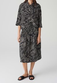 Mustavalkoinen mekko, jossa on raidallinen kuvio, ylisuurilla kauluksilla, kolmivarttisilla hihoilla ja kerätyllä vyötäröllä. Yhdistetty mustiin sandaaleihin.