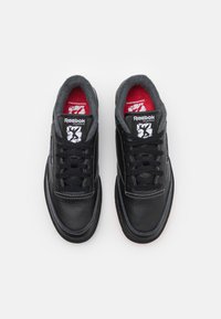 Černé kožené tenisky s šedým podšitím, kontrastním bílým prošitím a černými tkaničkami. Mají červenou stélku a logo Reebok Classic na jazyku.