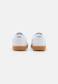 Fehér b�őr Nike sportcipők világoskék részletekkel, gumiból készült talppal és hímzett logóval a saroknál. Klasszikus alacsony szabású dizájn.