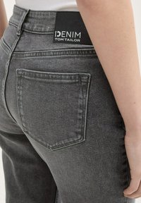 Jeans de mezclilla gris de cintura alta, con un bolsillo trasero y una etiqueta de cuero negra que dice "DENIM TOM TAILOR". Tela texturizada.
