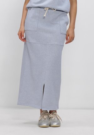Persoon draagt een lichtgrijze midi-rok met voorzakken en een voorzijde split, gecombineerd met zilverkleurige sneakers met beige veters.