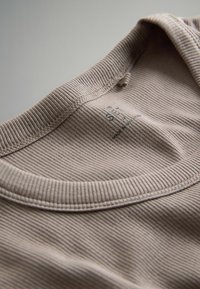 Beige geripptes T-Shirt mit Kragen und Nähdetails. Das Pflegeetikett innen liest "SET" und "MADE IN ANGULAS". Glatte Textur.