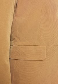 Ruskea muotitakki, jossa on sileä rakenne, jossa on yksi rintatasku ja hillityt saumat, suunniteltu muodolliseen käyttöön.