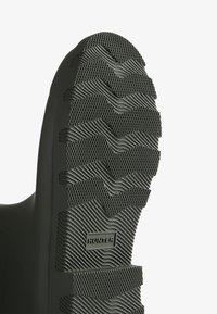 Semelle de botte en caoutchouc noir avec un motif de semelle texturée et ondulée, comprenant des grips directionnels et un logo de marque central "HUNTER" dans un format rectangulaire.