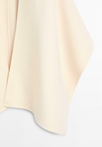 Beige pletený šál s měkkou texturou, disponující volným designem a splývavými okraji, ideální pro vrstvení.