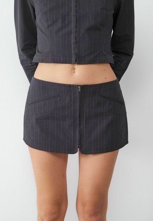 Schwarzes gepunktetes Crop-Top mit einem Reißverschluss an der Vorderseite und einem passenden, taillenhohen Minirock mit abgerundeten Taschen und einer glatten Oberfläche.