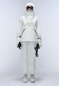 White snow jacket with a high neck, adjustable hood, and front logo patch. Paired with matching snow pants and insulated gloves.
