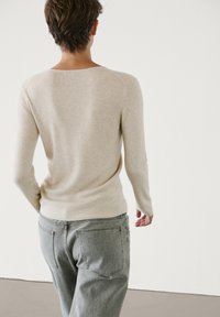 Beige geribbelde trui met lange mouwen, ronde hals, gecombineerd met grijze jeans. De textuur lijkt zacht en aansluitend bij de taille.