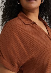 Camicia color ruggine con colletto, caratterizzata da un motivo testurizzato, con maniche corte e un tessuto leggero con un sottile effetto a coste.