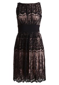 Robe sans manches longueur genoux avec superposition en dentelle florale noire et doublure nude, taille cintrée avec bande noire unie.