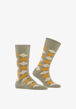 Grüne Socken mit einem Rautenmuster in Orange und Creme. Gerippter Abschluss und glatte Textur, mittellang bis zur Wade.