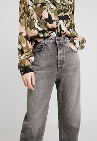 Vaqueros de denim gris de cintura alta con un corte relajado, que presentan costuras visibles y bolsillos. Combinados con una blusa de estampado floral en tonos terrenales.