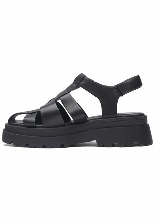 Sandales en cuir noir avec de larges brides croisées, orteils ouverts et semelle plate-forme épaisse avec un design texturé et cranté.