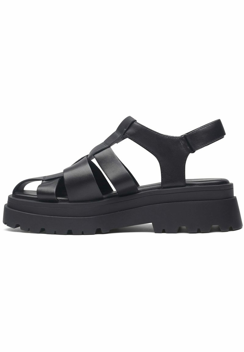 Sandales en cuir noir avec de larges brides croisées, orteils ouverts et semelle plate-forme épaisse avec un design texturé et cranté.