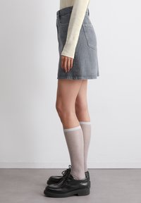 Grå stripete denimskjørt med høy midje, lagdelt over lysegrå knelange strømper, kombinert med svarte snør-sko.
