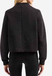 Felpa corta a costine nera con collo alto e cerniera sul retro. Le maniche lunghe si allungano fino ai polsini a costine. Materiale liscio e strutturato.
