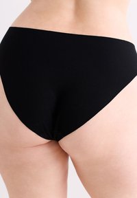Culotte taille haute noire en tissu lisse, avec un dos couvrant complètement et une forme arrondie. Le design sans coutures garantit qu'il n'y a pas de marques visibles sous les vêtements.