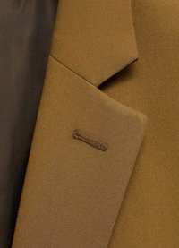 Brown tailored jacket featuring a textured fabric, sharp collar, and a small stitched logo detail on the pocket.