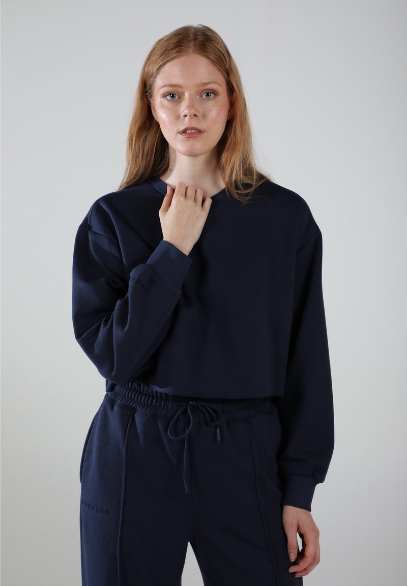 Navy Cropped-Sweatshirt mit langen Ärmeln, gerippten Bündchen und rundem Halsausschnitt, kombiniert mit passenden Jogginghosen mit Kordelzug und seitlichem Logo.