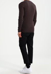 Pull en maille marron côtelée à manches longues, coupe ajustée et col rond, associé à un pantalon noir fuselé et des baskets blanches.