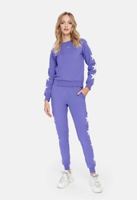 Paarse sweatshirt en bijpassende joggers van zachte stof; sweatshirt heeft witte steraccenten op de mouwen, elastische tailleband op de broek.
