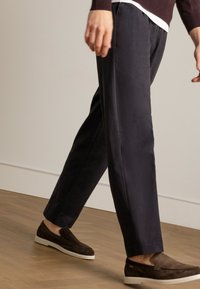 Marineblauwe broek met een rechte snit, gemaakt van zachte stof, met een soepele textuur. Gecombineerd met donkerbruine instappers op een houten vloer.