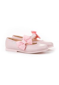 Un par de zapatos Mary Jane para niños pequeños en rosa claro con grandes lazos de tela rosa en las correas, suelas planas y un acabado suave.