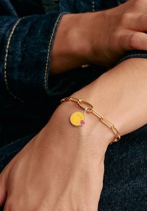 Goldene Kettenarmband mit einem gelben lächelnden Anhänger und einem Herz. Die Kette hat verlängerte Glieder und eine polierte Oberfläche.