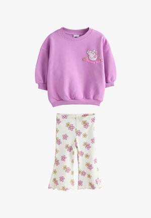Lille barn med blondt hår iført en lilla sweatshirt med en tegneseriegris og hvide bukser med lyserøde og gule blomster.