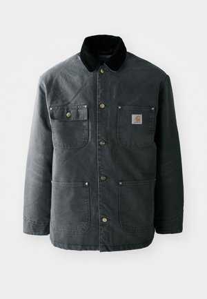 Chaqueta de lona gris oscuro con un cuello de pana negro, botones de presión de latón y dos bolsillos en el pecho con un parche de logo. Textura suave.