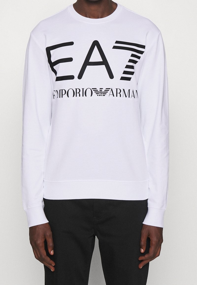 Vit sweatshirt i bomull med svart grafisk text "EA7 EMPORIO ARMANI" i olika stilar. Ribbad mudd och nederkant.