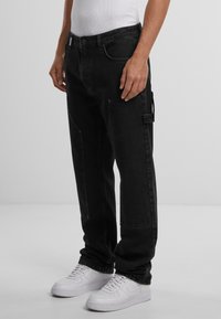 Sorte denim cargo bukser med en afslappet pasform, sidelommer og syninger, parret med hvide sneakers.