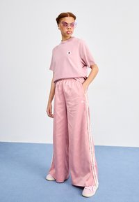 Rosa oversized t-shirt med liten logotyp, kombinerad med lösa satinrosa byxor med vita sidostripes och matchande rosa sneakers.